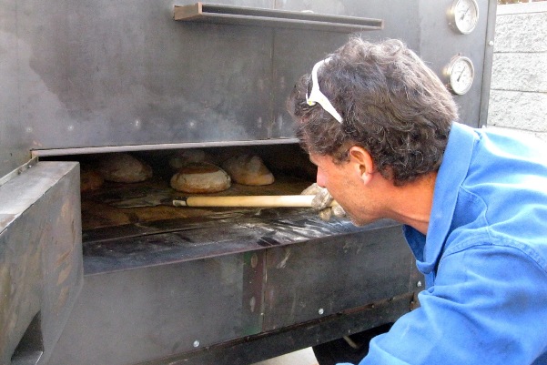 Michael O’Malley checks on bread in his mobile bread oven at Grist & Toll. Credit: Amy Halloran